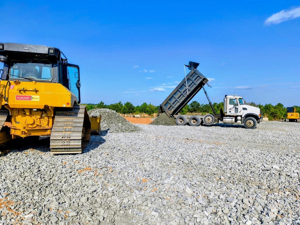 Dump truck delivering aggregate at an active construction site with heavy equipment on site