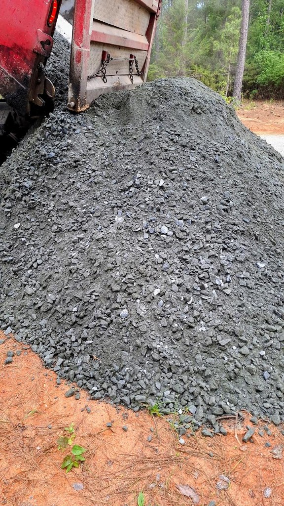 Dump truck tailgate tipping crushed stone aggregate onto a job site pile