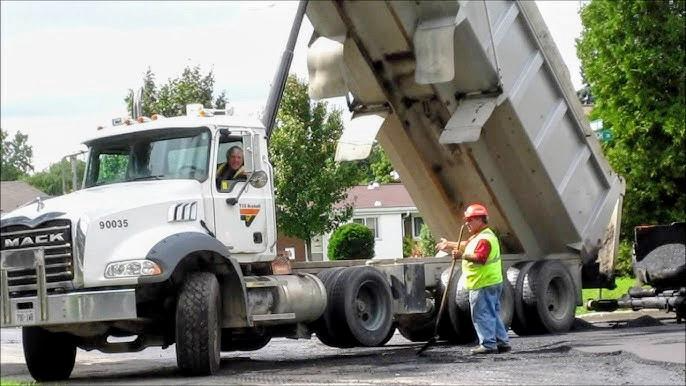 White Mack dump truck discharging material at a residential site with a worker in safety gear
